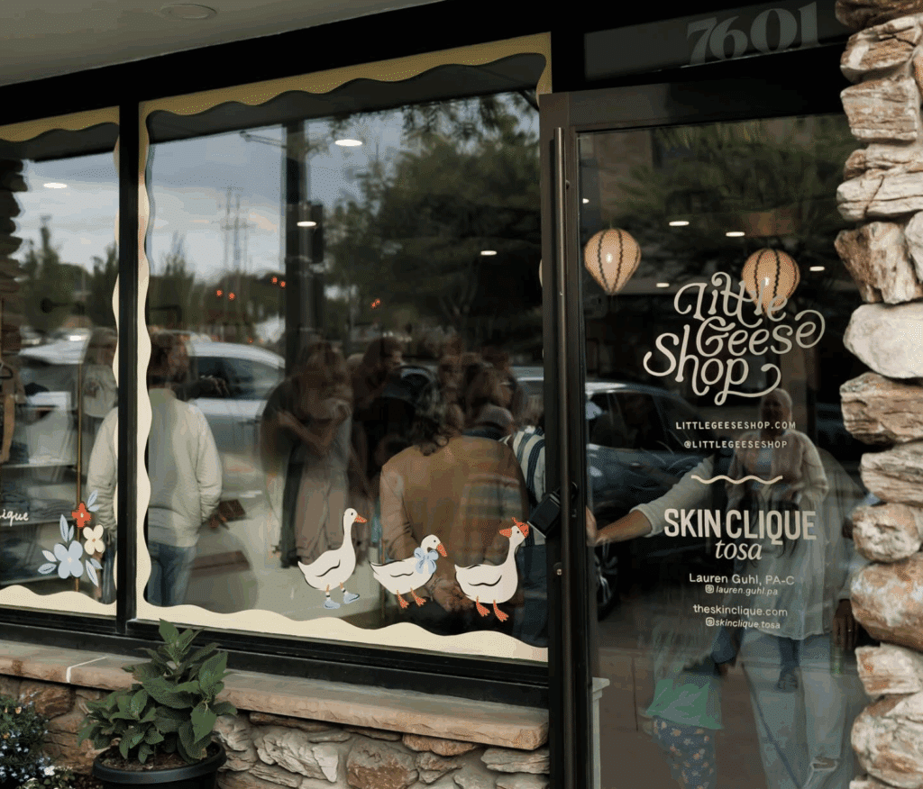 Exterior of The Little Geese Shop with three white geese window decals and glass door partially open.
